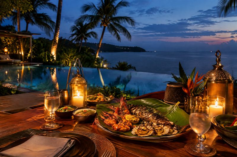 Candlelit dinner table beside the pool with grilled seafood at blue hour